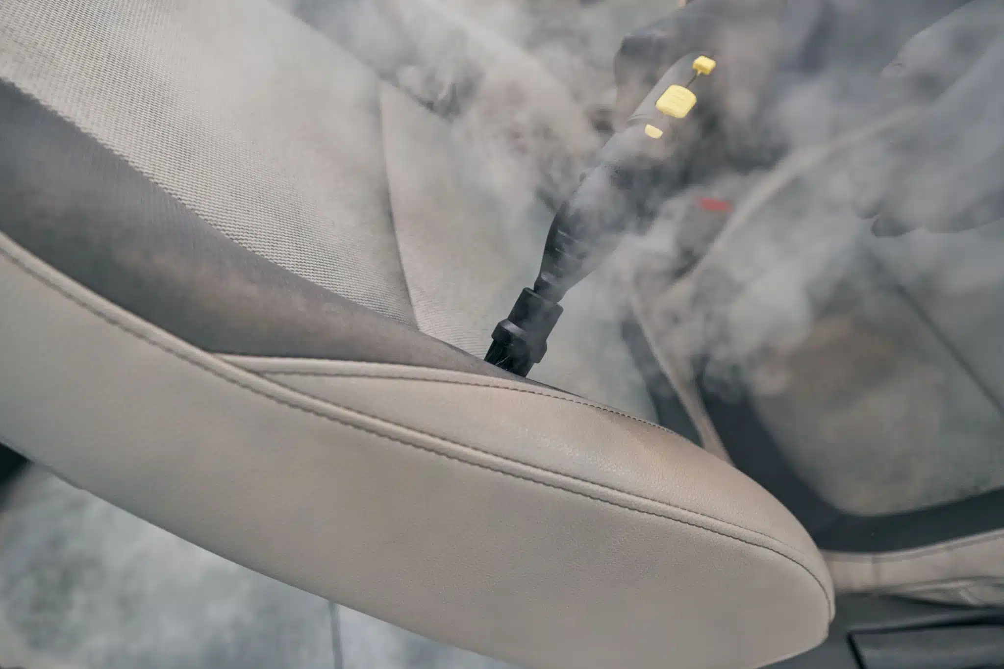 High-quality image of professional steam cleaning equipment being used on luxury car interior, showing detail-oriented work on leather seats and dashboard
